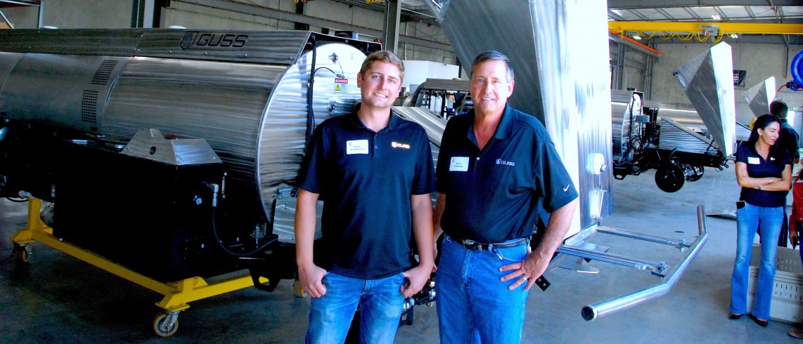 two men in front of an automated farm spraying rig