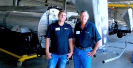 two men in front of an automated farm spraying rig