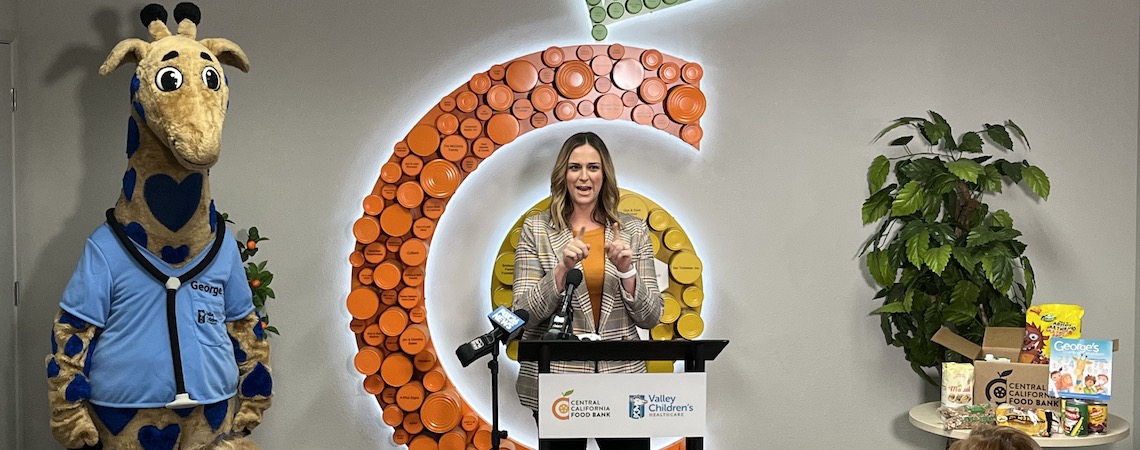 woman at a podium with a giraffe mascot to her right