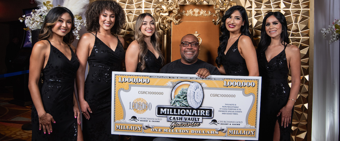 man seated with oversized check, surrounded by women