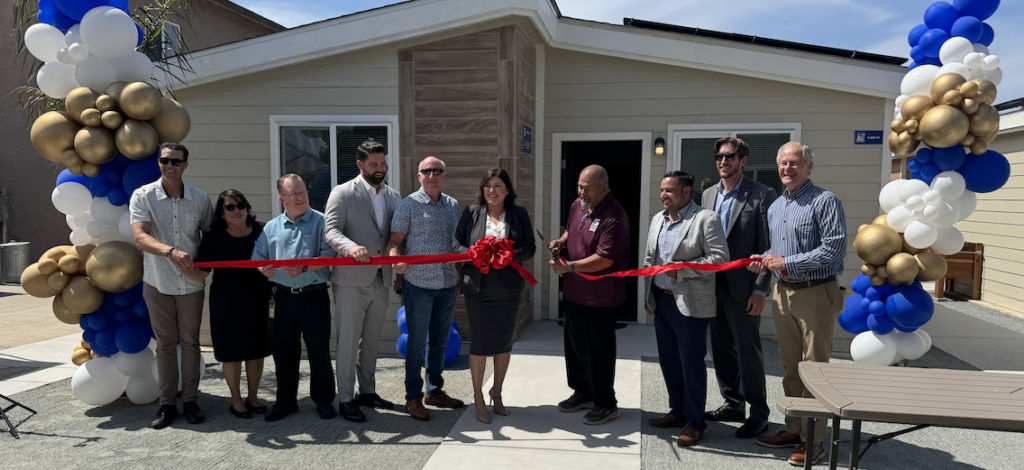 ribbon cutting with several people in front of a tiny home
