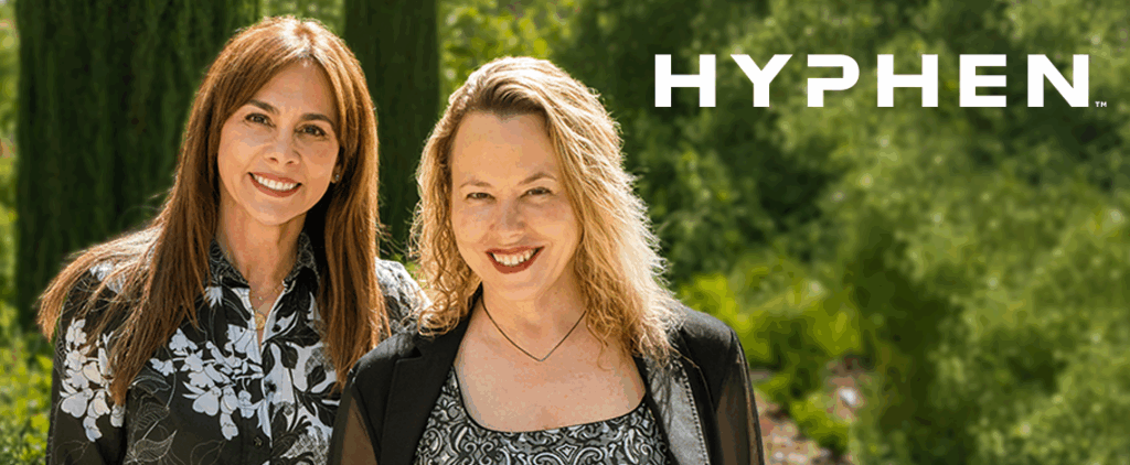 two women smiling with the word "hyphen" over their shoulder