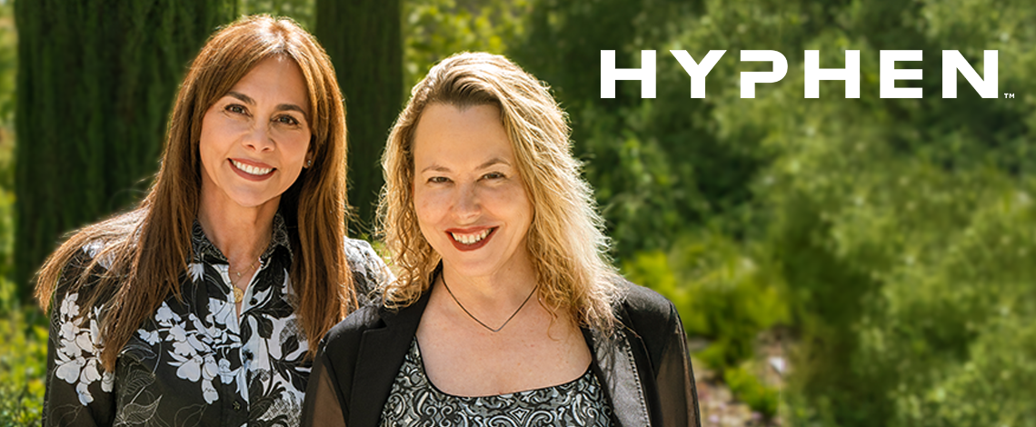 two women smiling with the word "hyphen" over their shoulder