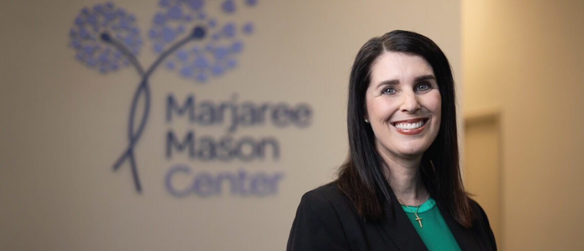 woman smiling in front of wall sign that reads "marjaree mason center" with stylized dandelions