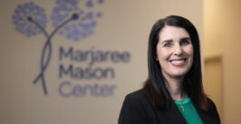 woman smiling in front of wall sign that reads "marjaree mason center" with stylized dandelions