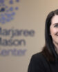 woman smiling in front of wall sign that reads "marjaree mason center" with stylized dandelions