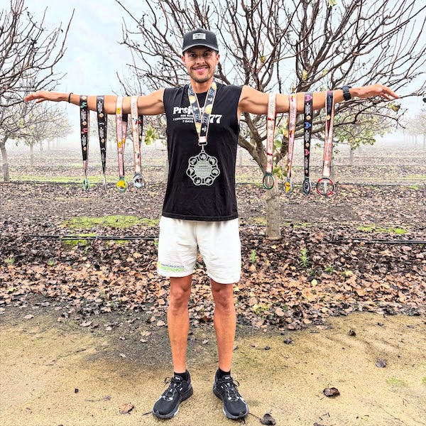 man in a t pose with athletic medals on his chest and slung on his arms