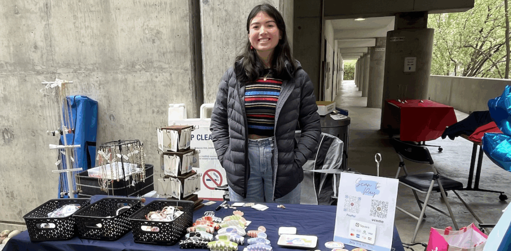 a woman standing in front of a table with beads and stickers for sale