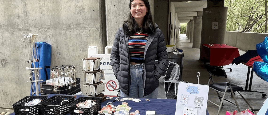 a woman standing in front of a table with beads and stickers for sale