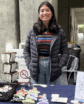 a woman standing in front of a table with beads and stickers for sale