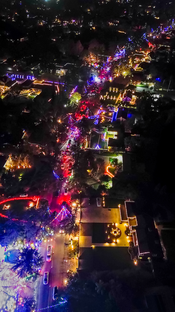 a long street with homes with bright xmas displays, aerial view