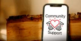 a phone with the community support logo on the screen, proped up on a log