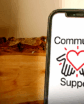 a phone with the community support logo on the screen, proped up on a log