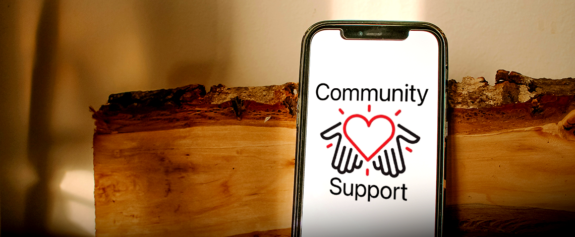 a phone with the community support logo on the screen, proped up on a log