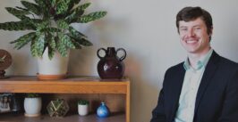 man smiling as he sits next to a book shelf
