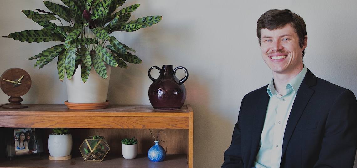 man smiling as he sits next to a book shelf