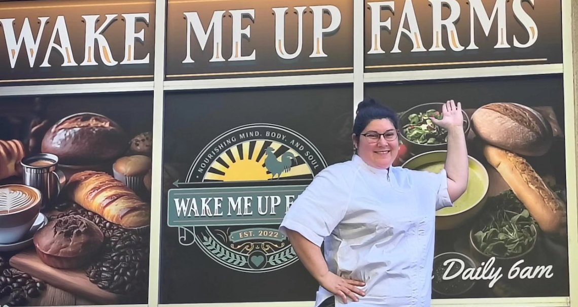 a woman pointing to a wall art sign that says wake me up farms and features loaves of bread