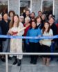 a group of people preparing to cut a blue ribbon in front of a newspaper building