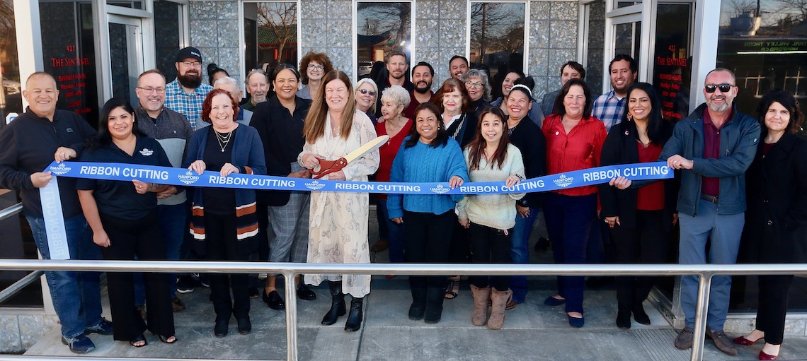 a group of people preparing to cut a blue ribbon in front of a newspaper building