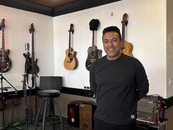 man in front of a wall with mounted guitars