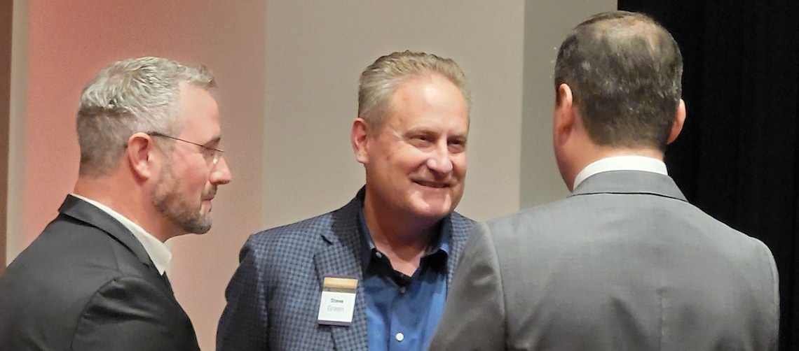 three men speaking, one with their back to the camera, the other in profile