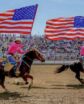 two riders on horses holding U.S. flags