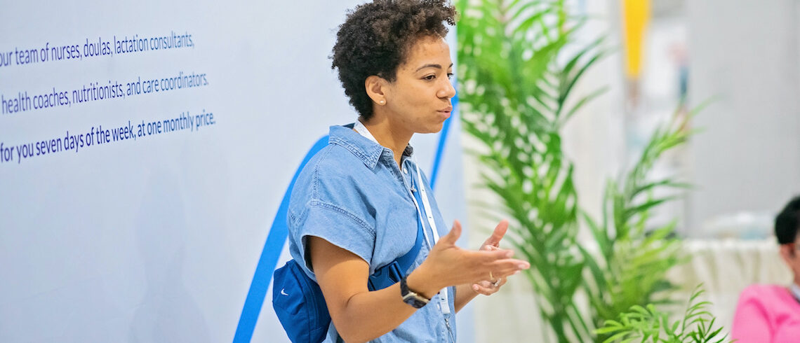 a woman speaks in front of a wall