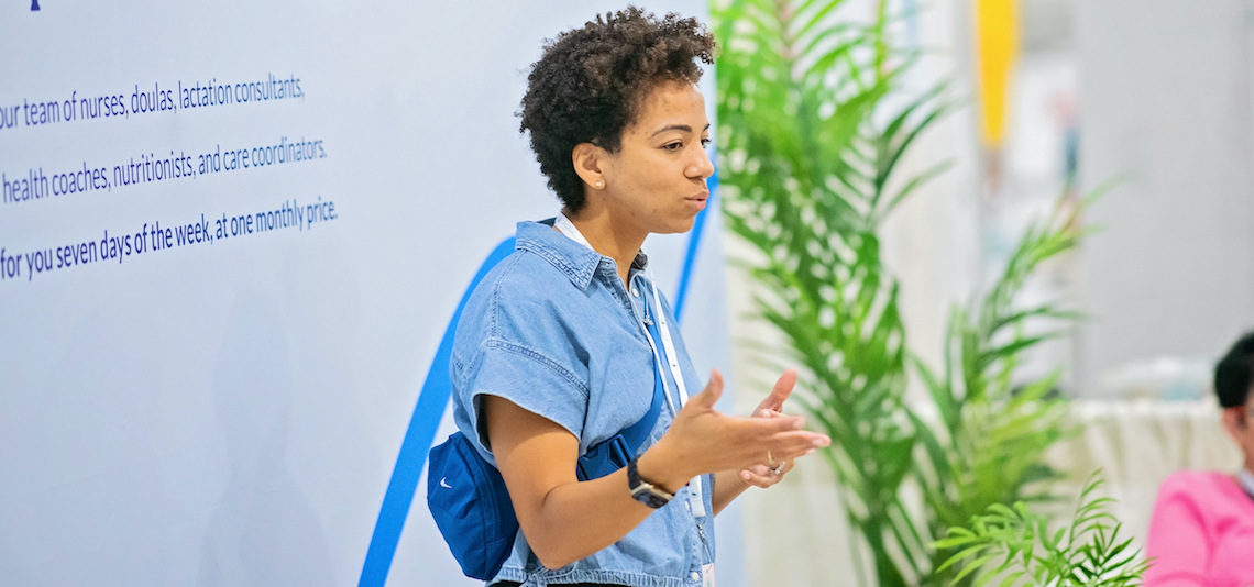 a woman speaks in front of a wall