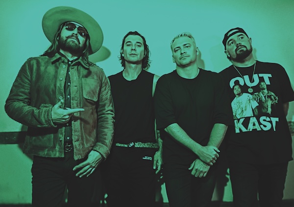 four guys in a band leaning against a wall