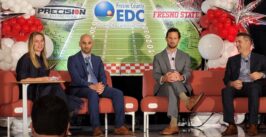 four people seated on a stage with a football stadium backdrop with balloons
