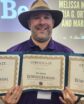man in cool hat holds three certificates
