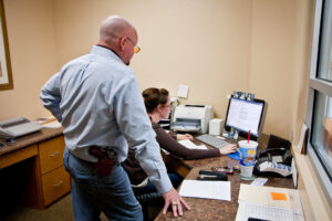 man standing over a woman's shoulder looking at a computer screen