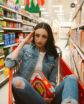 woman in a shopping basket in a grocery store aisle holding lucky charms