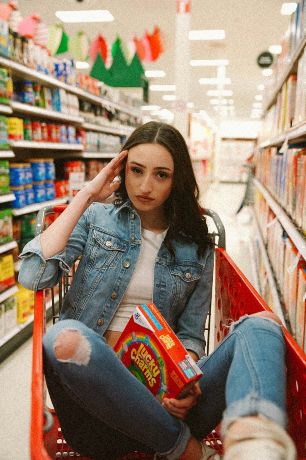 woman in a shopping basket in a grocery store aisle holding lucky charms