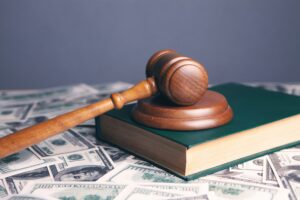 Wooden judge's gavel resting on a law book atop U.S. $100 bills.