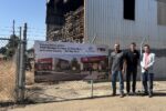 Three men stand beside a chain-link fence in front of a banner showing a rendering of the future Del Rey Boys & Girls Club.