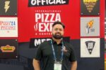 Valhinder Malhi of Curry Pizza Co. stands in front of an International Pizza Expo display.