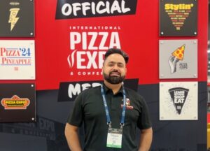 Valhinder Malhi of Curry Pizza Co. stands in front of an International Pizza Expo display.