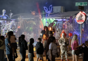 Visitors walk past a Halloween yard display with colored lights, artificial fog and people dressed as horror movie characters.